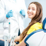 Brunette young woman in a yellow shirt smiles while sitting in the dental chair